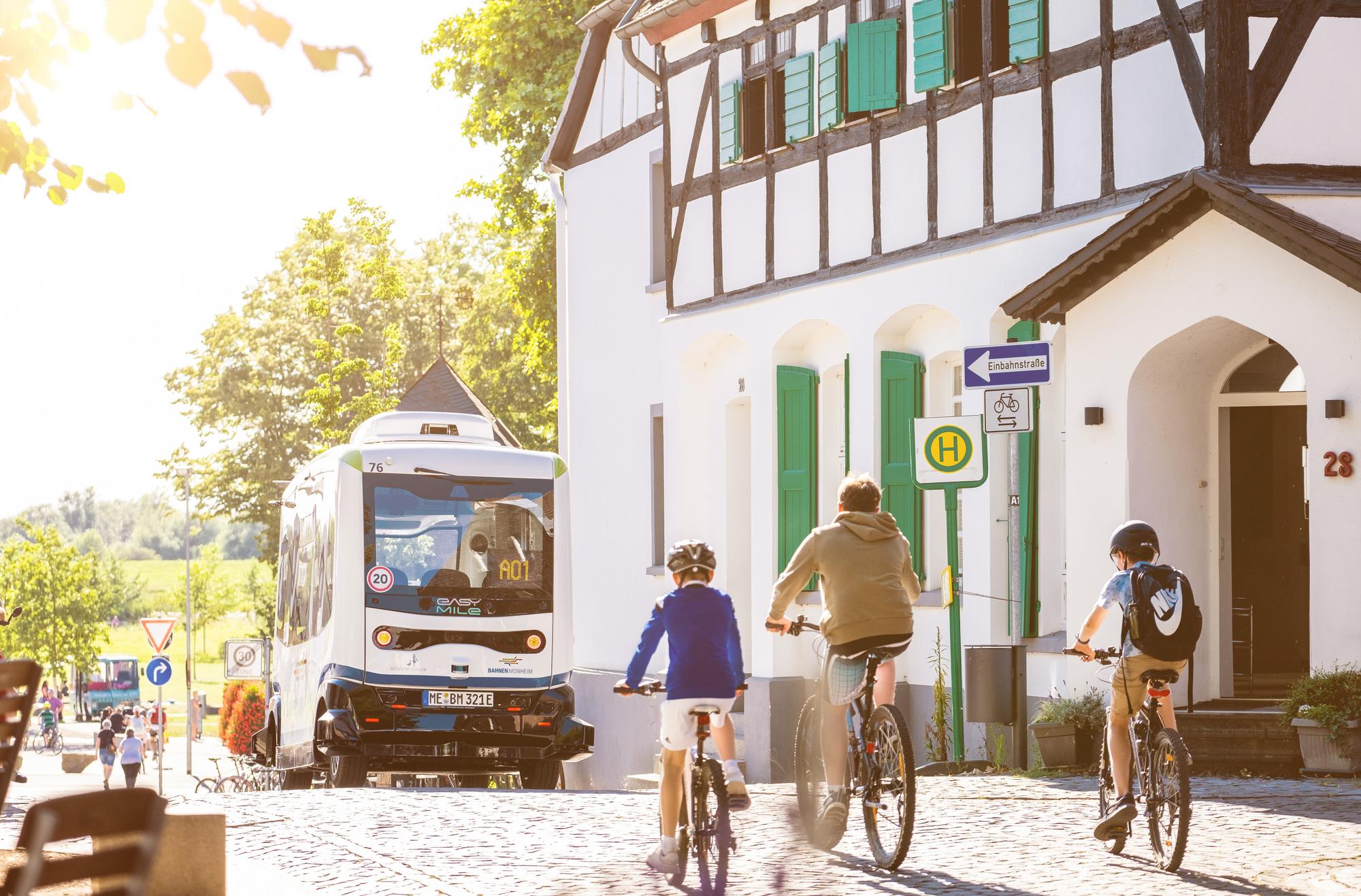 Drei Menschen fahren in der Monheimer Altstadt hinter dem autonomen Bus auf dem Fahrrad.