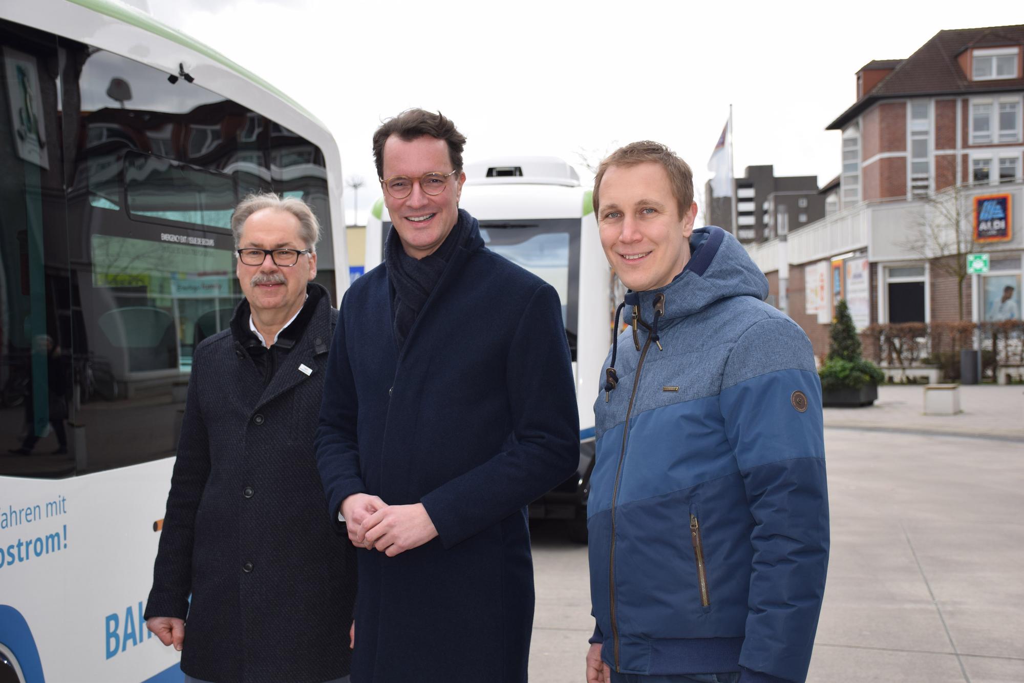 Drei Männer stehen in Monheim Mitte vor zwei autonomen Bussen.