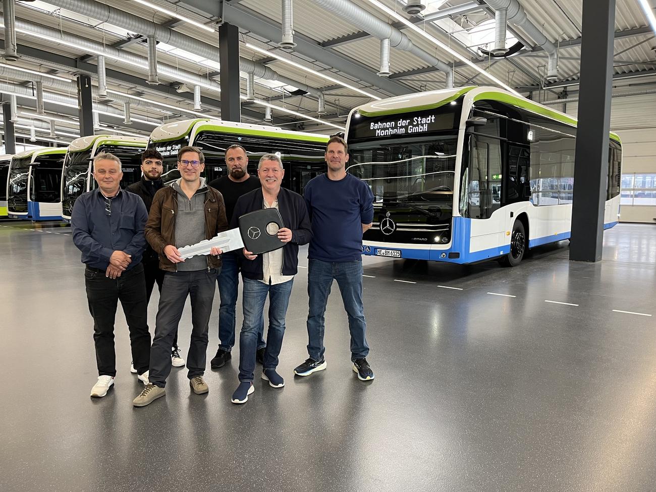 6 Personen stehen vor den neuen E-Bussen in einer Fahrzeughalle