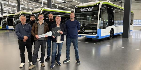 6 Personen stehen vor den neuen E-Bussen in einer Fahrzeughalle
