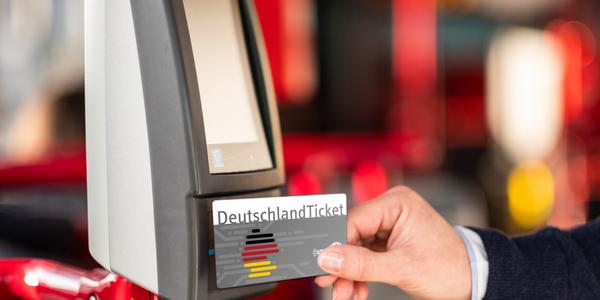 Eine Hand hält eine DeutschlandTicket-Chipkarte an das Lesegerät in einem Bus.